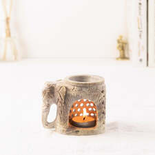 Soapstone aroma diffuser made into the shape of an elephant with delicate lattice work with tealight candle placed inside it and placed on the table with dried flower at the left with books and figurine at the right side white background.